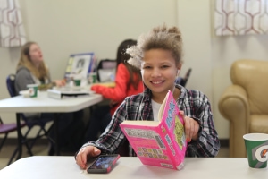 A preteen sitting at a desk with a pink book in her hand