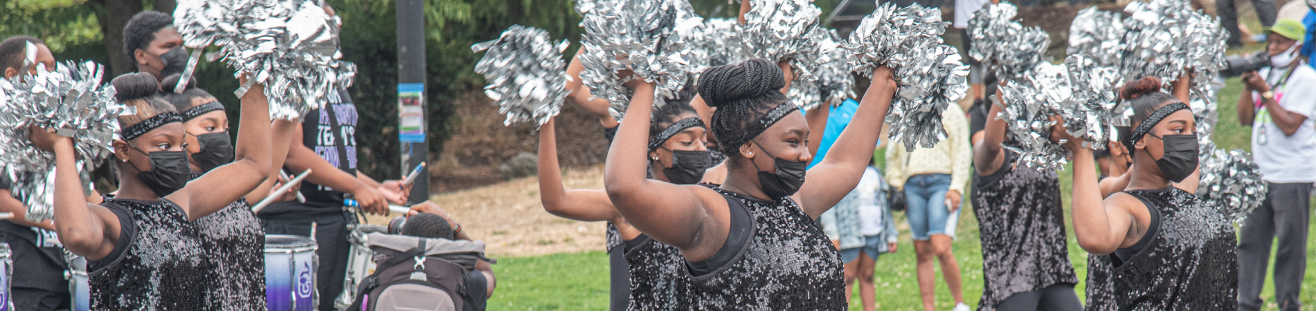group of women dressed in black, wearing face masks and holding silver pompoms