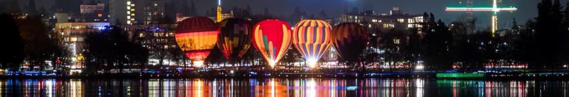 Hot air balloons resting near water at night lit up by city lights