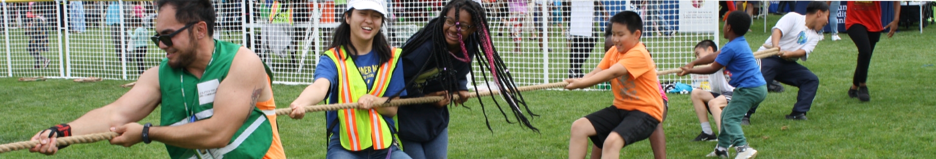 Parks and Recreation employees and children pulling a rope in tug of war in Rainier Playfield